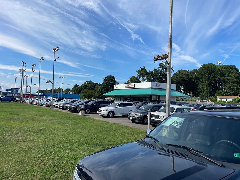 Cars parked at a car dealership on a sunny day with a blue sky and green grass.