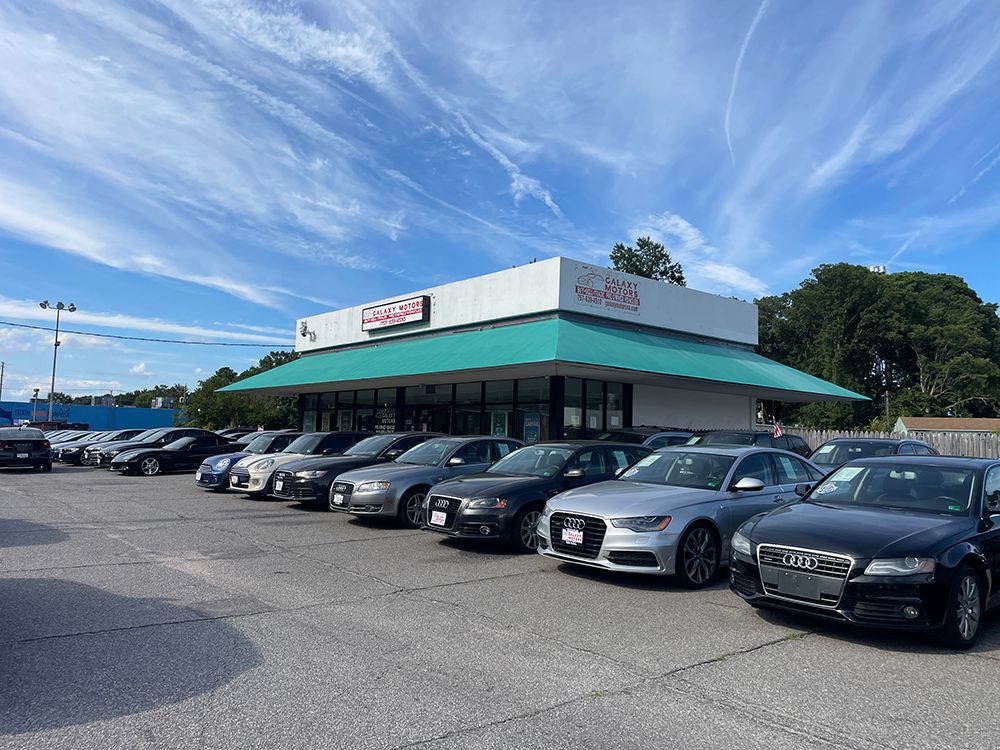 A car dealership with various cars parked in front of a single-story building under a blue sky.