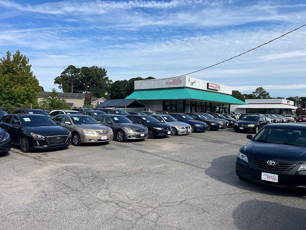 Cars parked in front of a car dealership with a green roof on a sunny day.