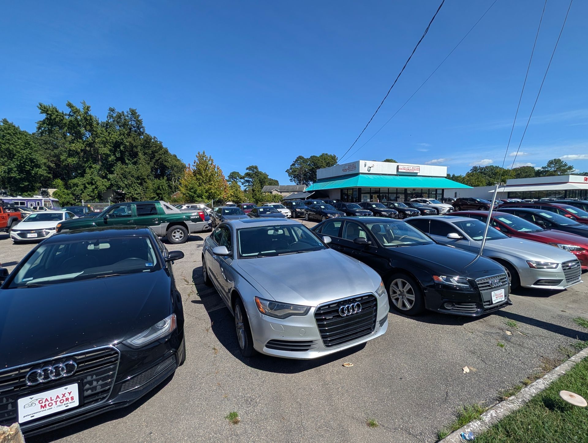 Parking lot with rows of parked cars under a clear blue sky near a low building.