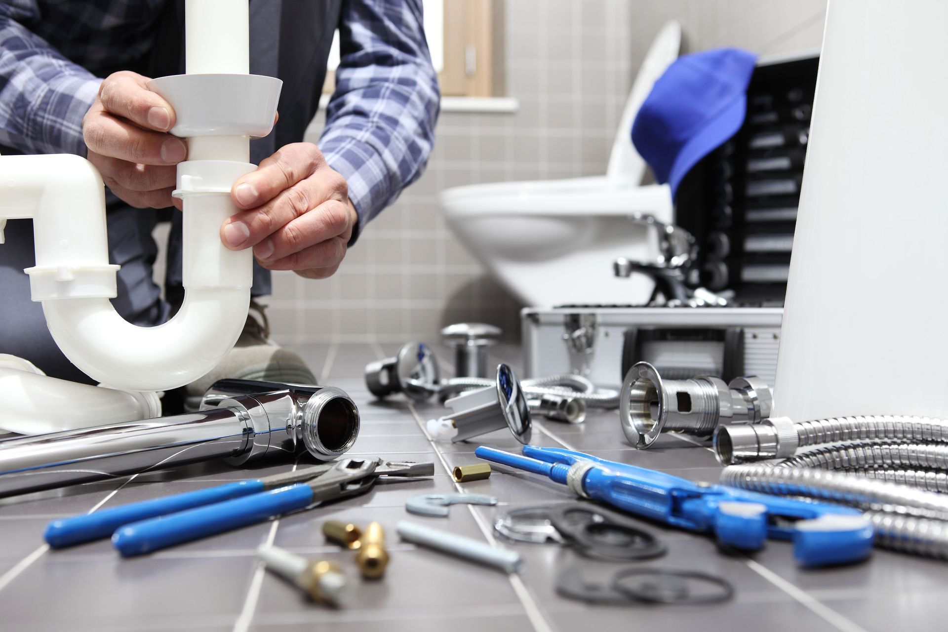Hands assembling white plumbing pipes on a workbench with blue tools and fittings nearby