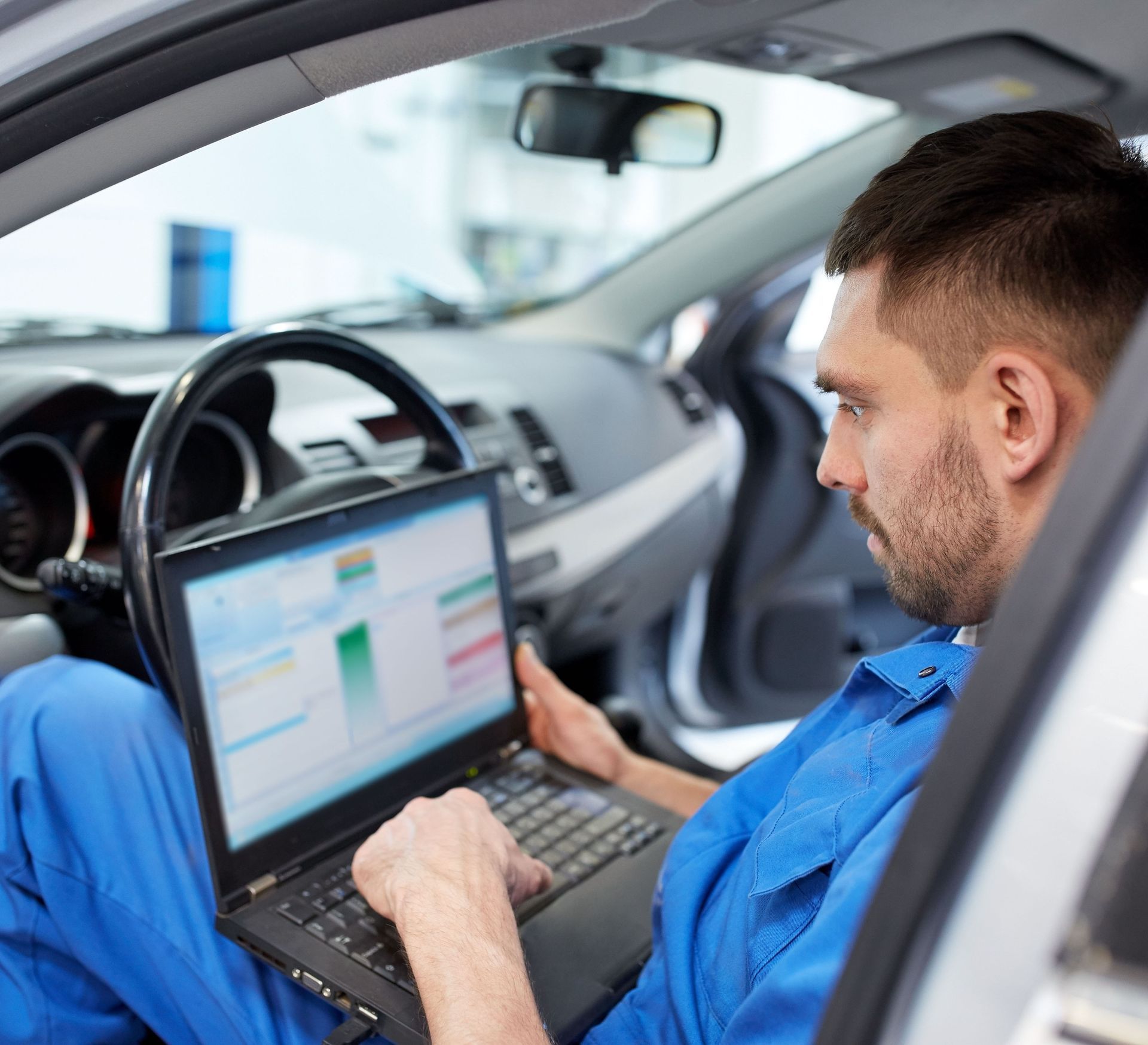Mechanic using a laptop inside a car for ADAS recalibration
