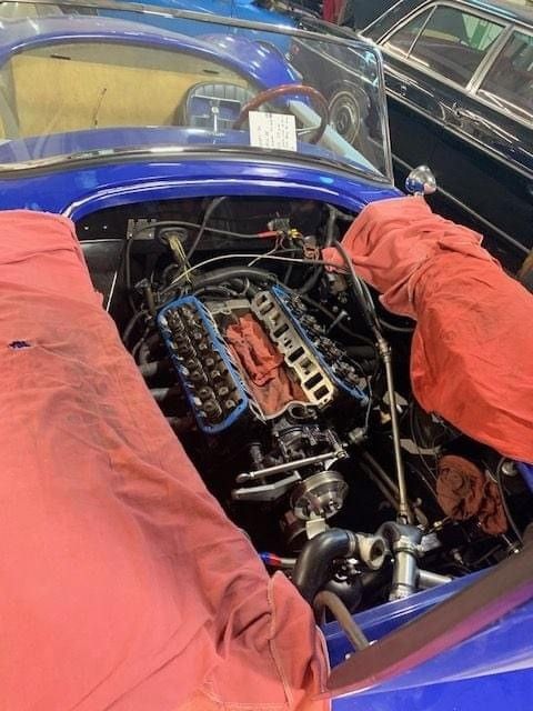 The engine of a blue car is covered with a red cloth