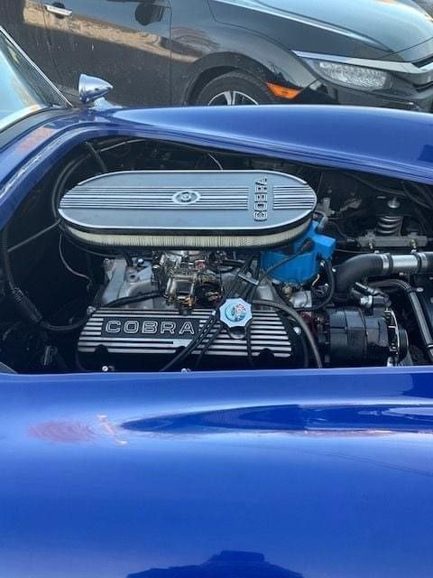 A blue car with a cobra engine is parked in a parking lot