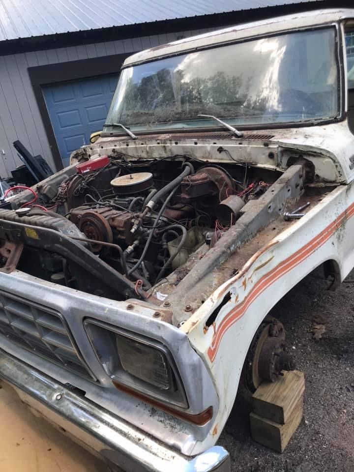 A white truck with the hood up is parked in front of a garage.