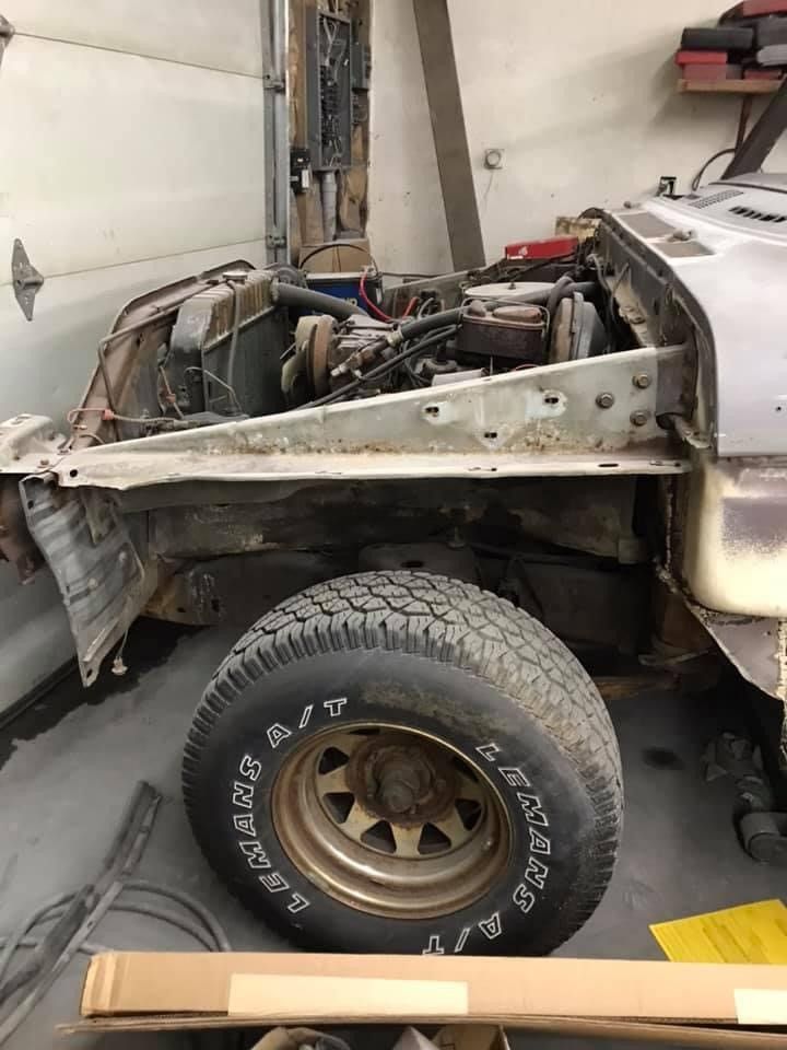 A jeep is sitting in a garage with the hood up and a tire on the ground.