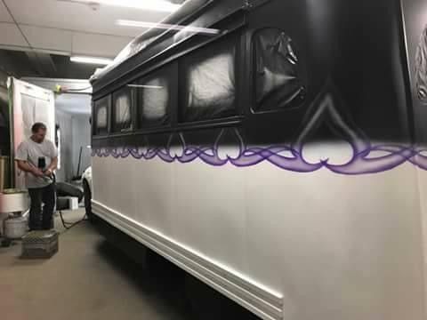 A man is painting a bus with purple hearts on it.