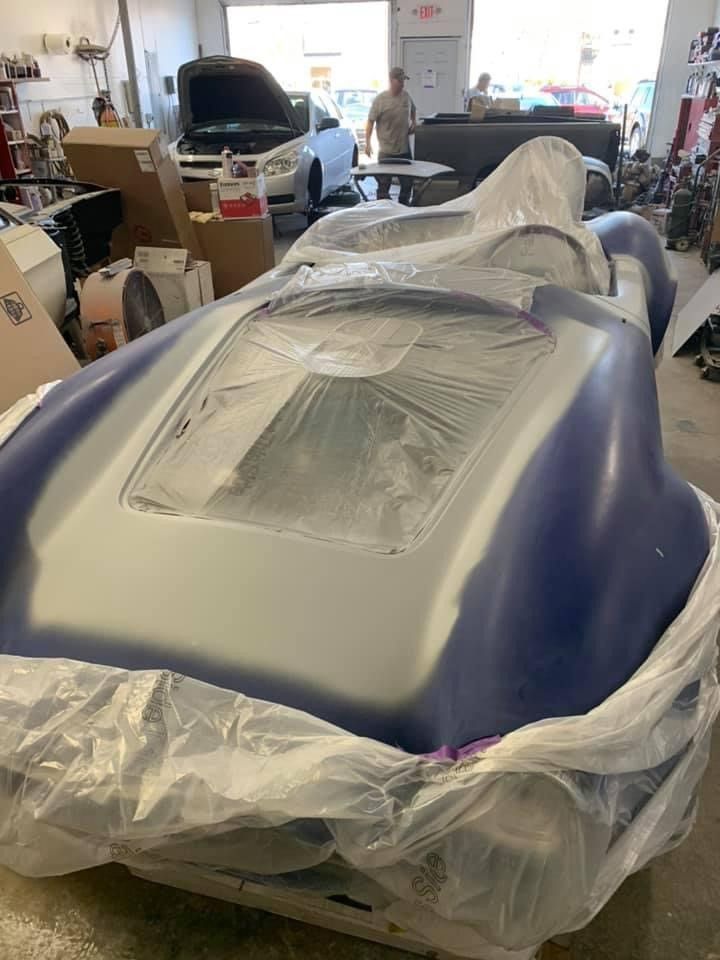 A blue and white sports car is wrapped in plastic in a garage.