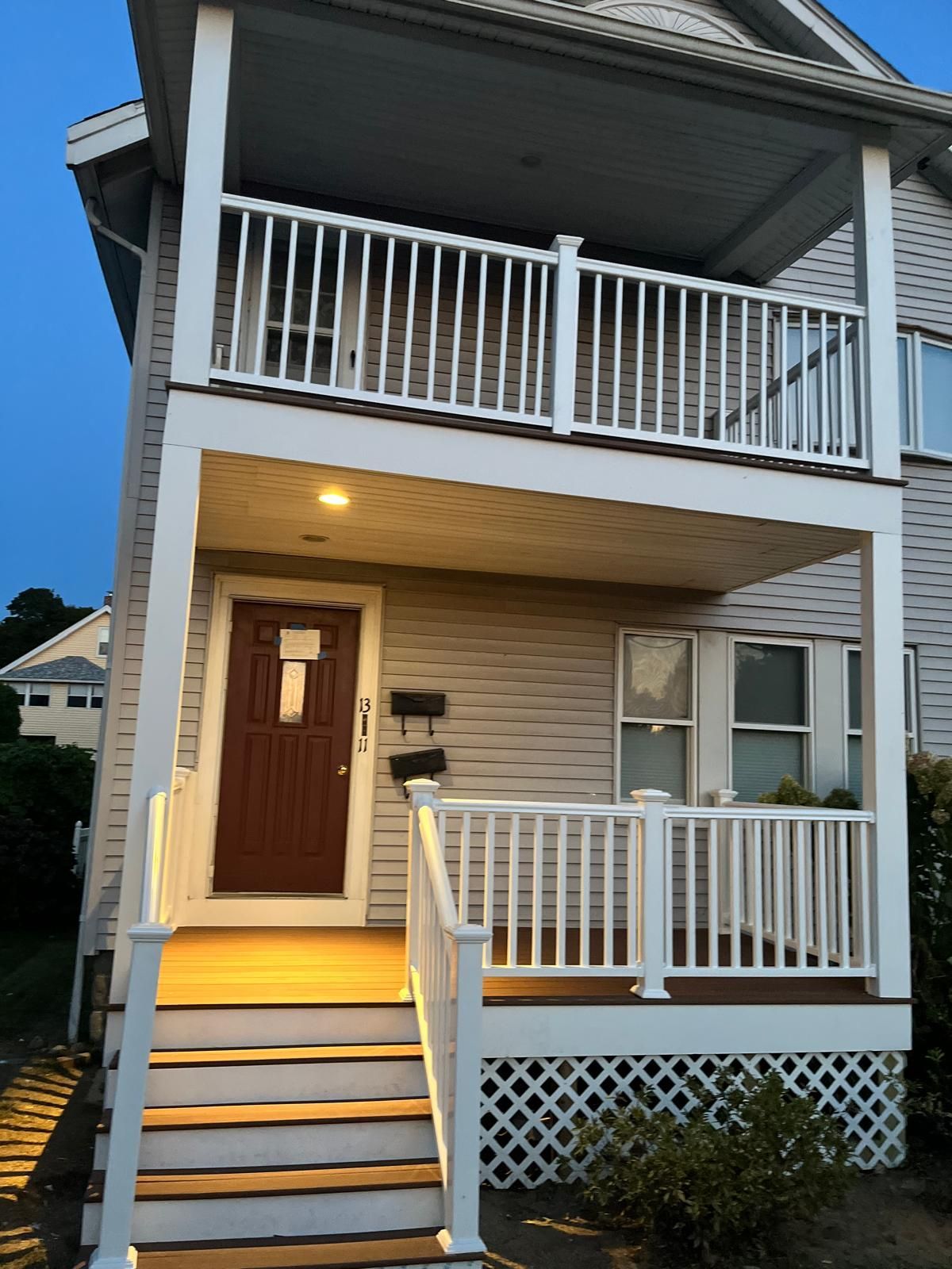 Two-story house exterior at dusk with lit front steps, white railings, and a brown front door