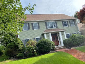 Two-story pale green house with white columns, red front door, and manicured lawn in front yard