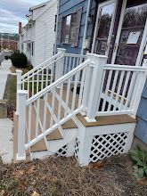 Front porch with white railings and stairs on a blue house, with lattice skirting underneath.