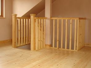 Wooden baby gate enclosure at top of stairs in a light wood-floored room