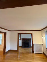 Empty living room with hardwood floors, white walls, and a dark fireplace centered on the far wall.