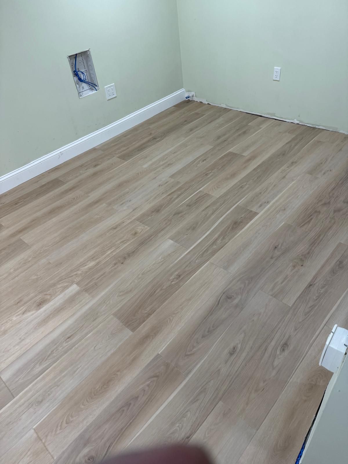 Empty beige room with wood laminate floor and a wall outlet opening.
