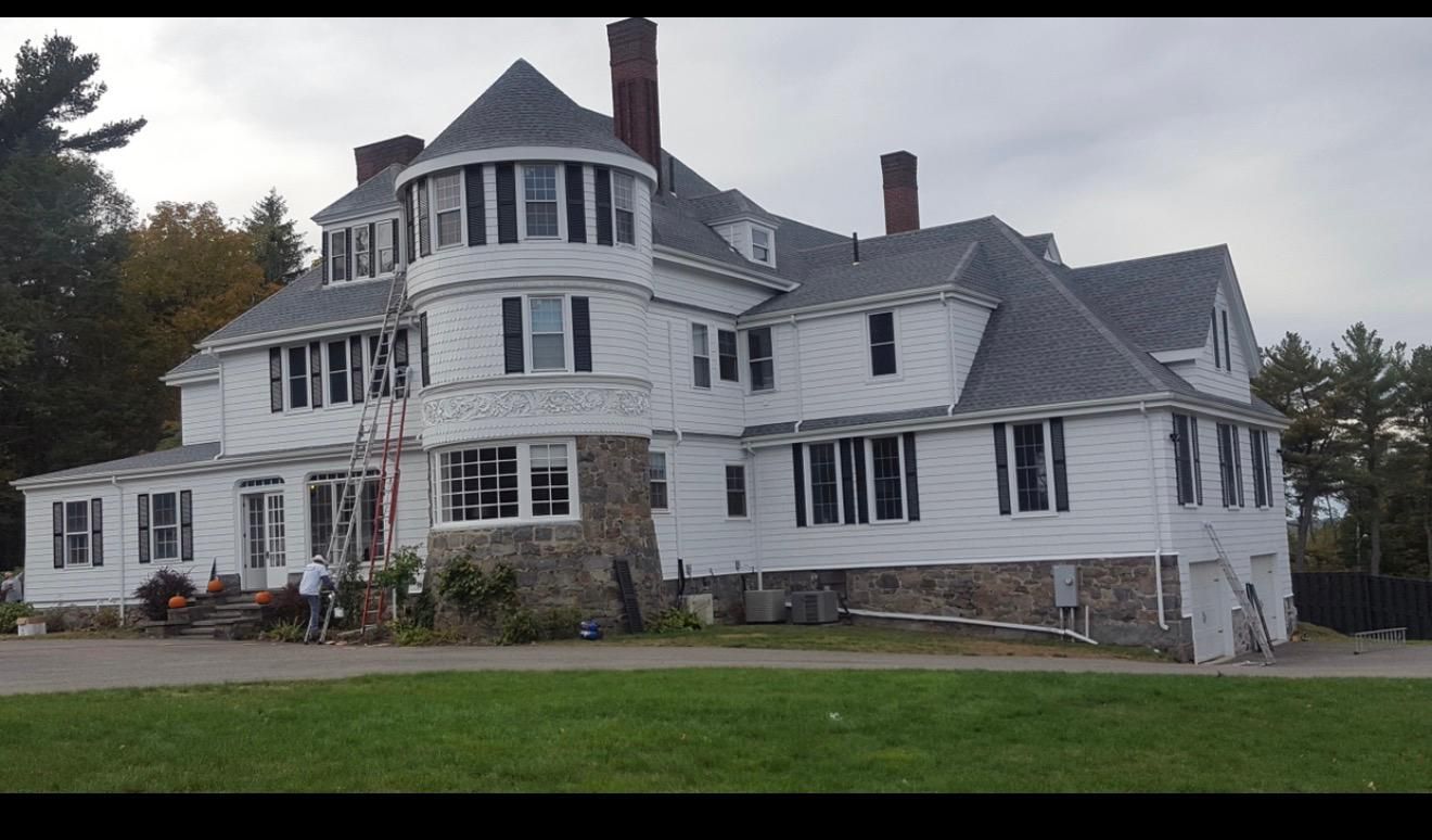 Large white Victorian-style house with a turret and gray roof on a grassy lawn under cloudy skies