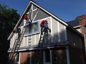 Workers on ladders painting the exterior of a house with light gray siding.