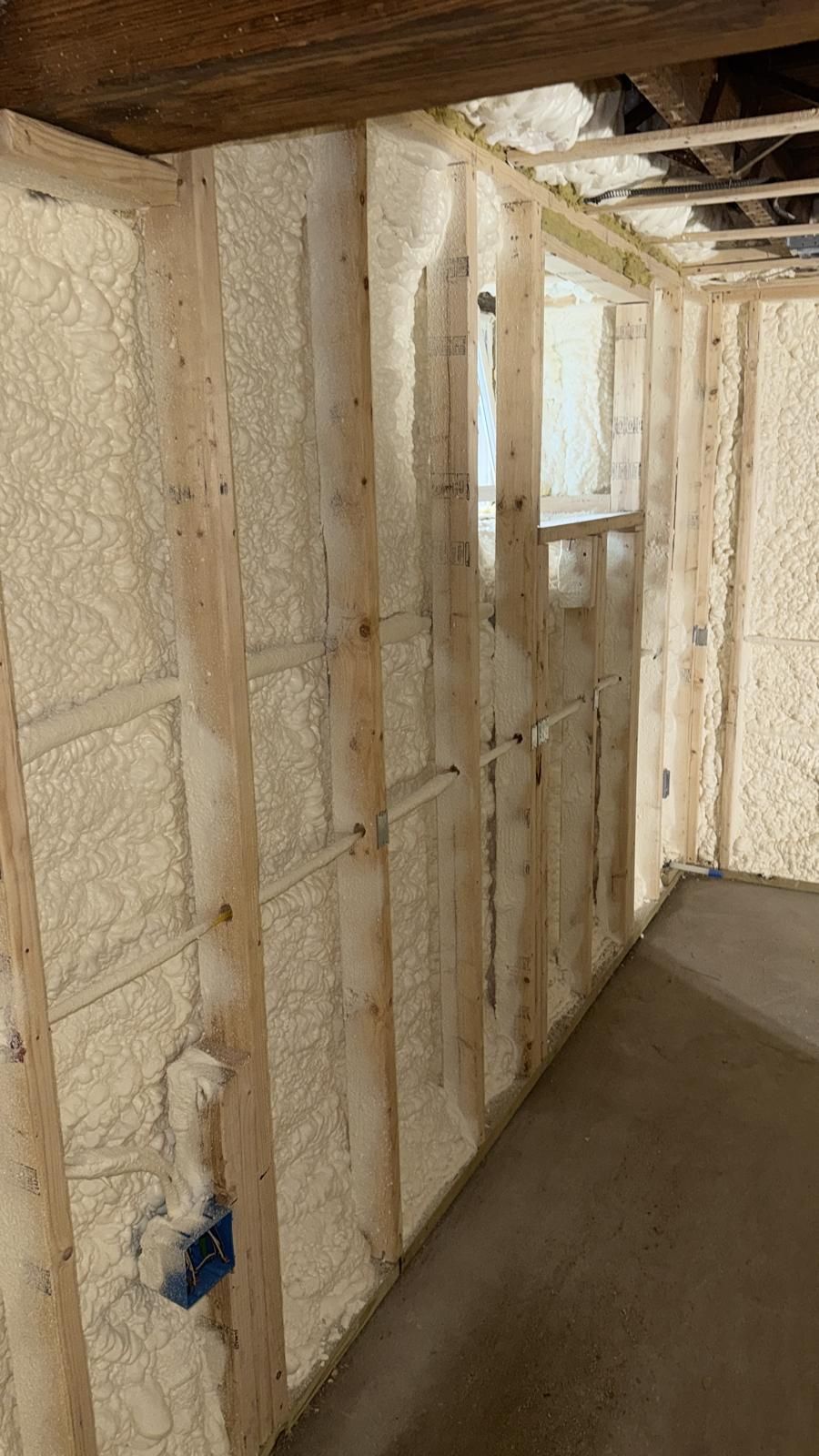 Insulated unfinished hallway with exposed studs, foam walls, and a small window opening