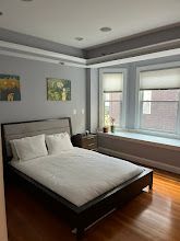 Modern bedroom with a dark wood bed, white bedding, gray walls, and two windows letting in daylight.
