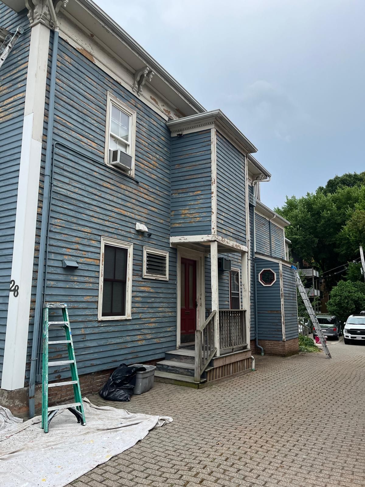 Blue two-story house with white trim, a front porch, ladder, and gravel driveway under construction.