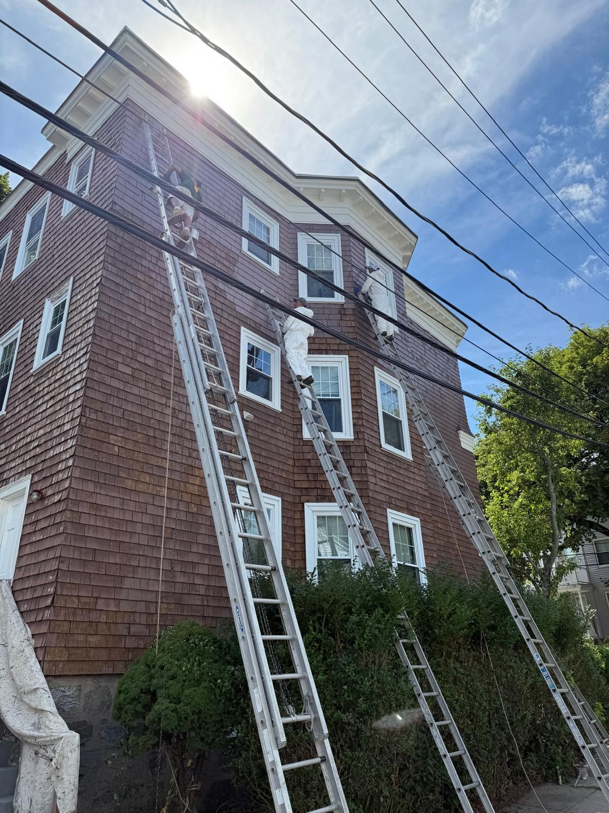 Brick apartment building with several extension ladders leaning up to windows under a blue sky