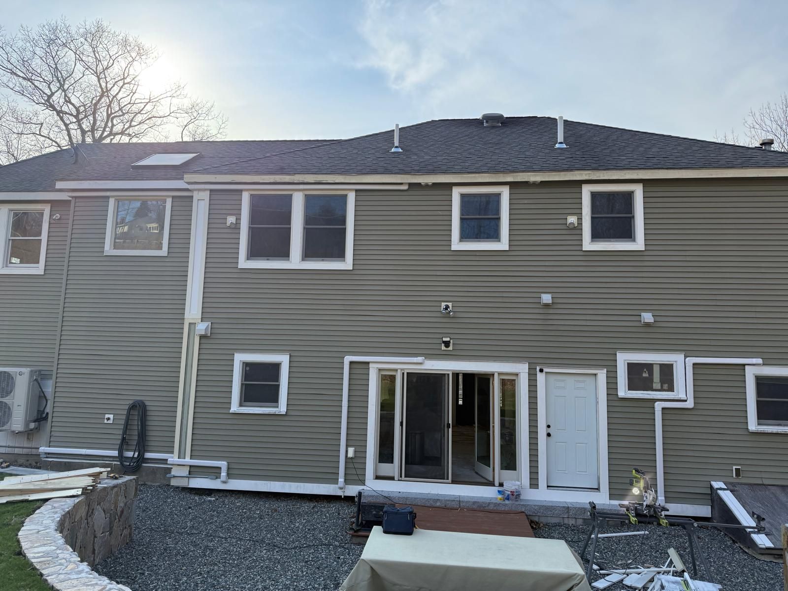 Back of a gray two-story house with sliding glass doors and small basement windows in winter.
