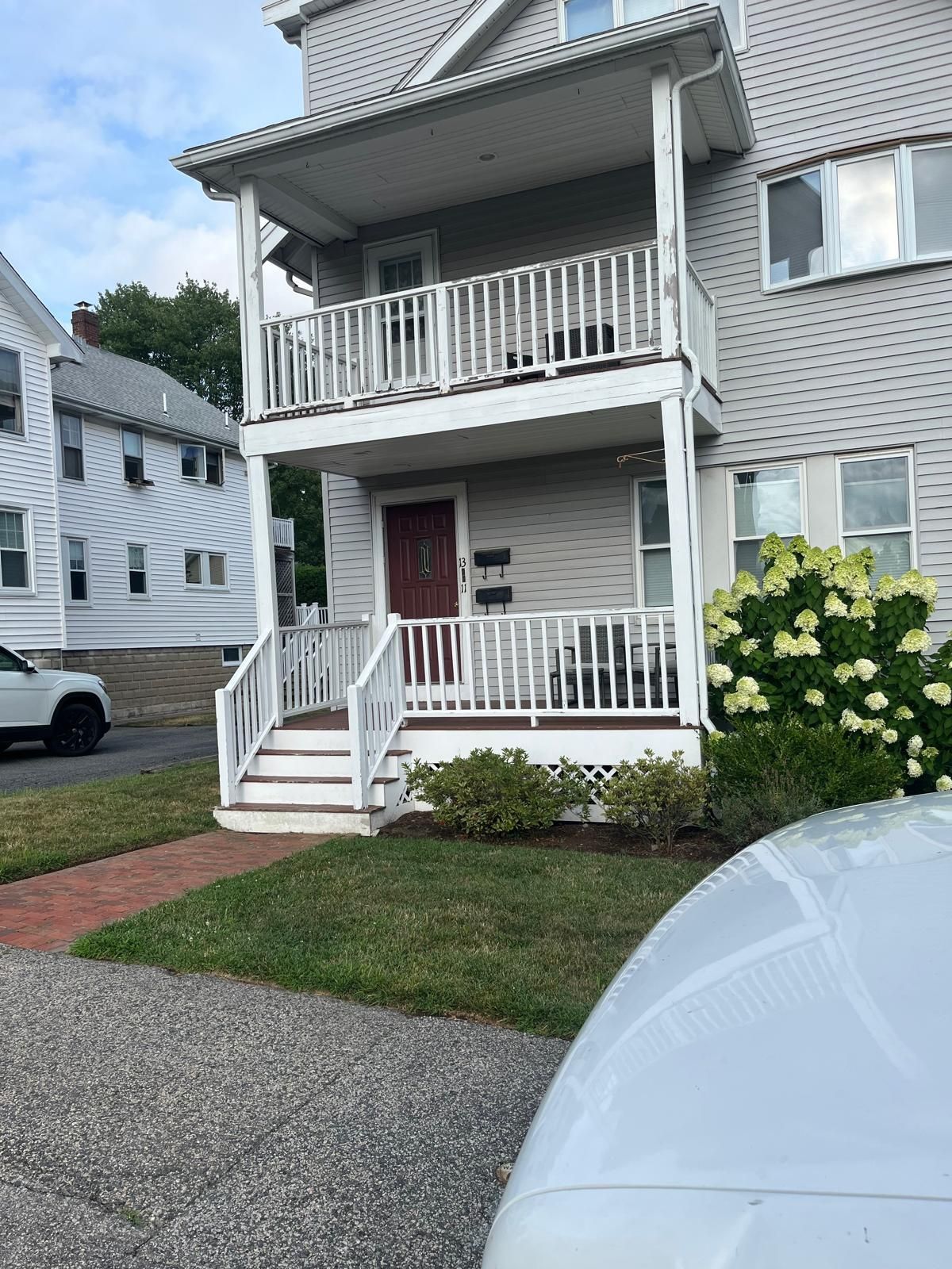 Two-story gray townhouse with white trim, red front door, and porch, seen from the driveway.