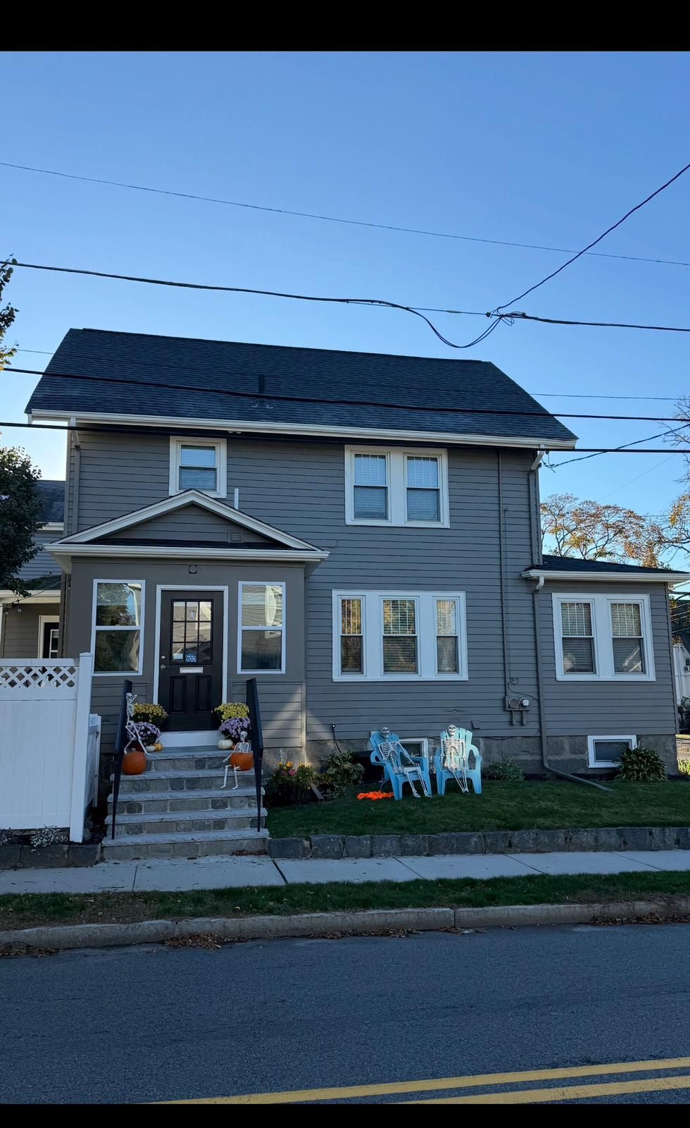 Gray two-story house with front porch, steps, white trim, and lawn chairs by the sidewalk.