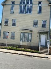 Three-story beige townhouse with white trim, front steps, and a white front door on a residential street.