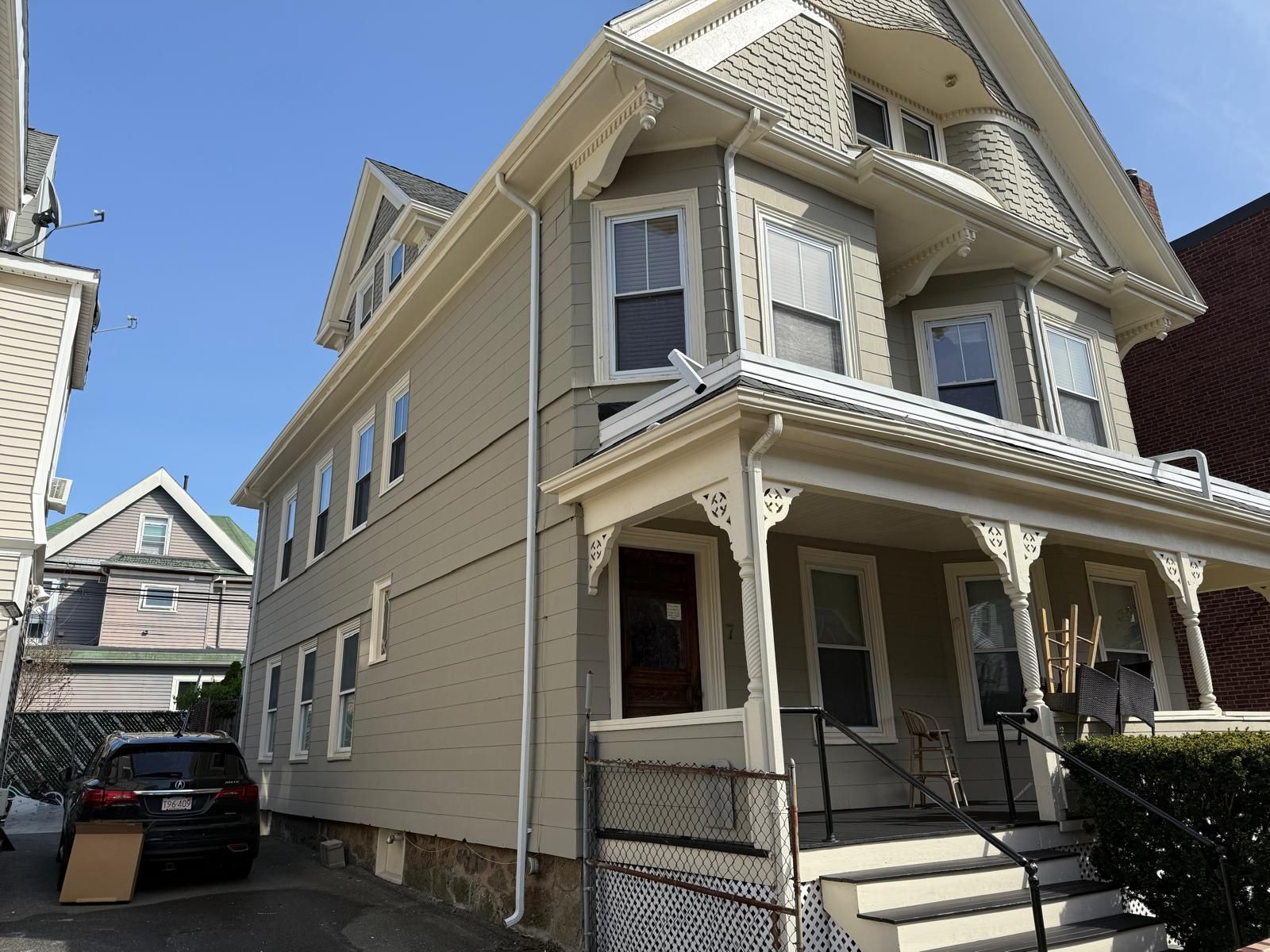 Beige two-story house with a covered porch and steps, viewed from the front corner on a sunny day