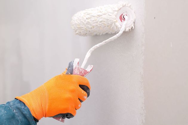 Person in orange glove painting a white wall with a paint roller