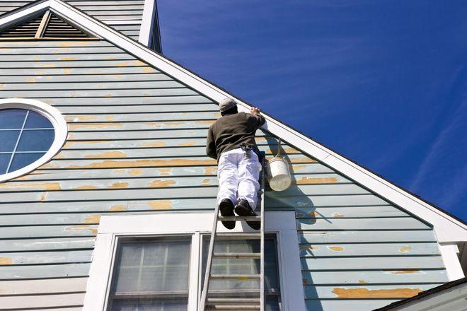 Painter on ladder painting light-blue house exterior under a blue sky