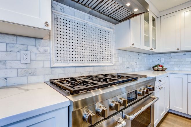 Modern white kitchen with stainless steel gas range, marble backsplash, and under-cabinet lighting