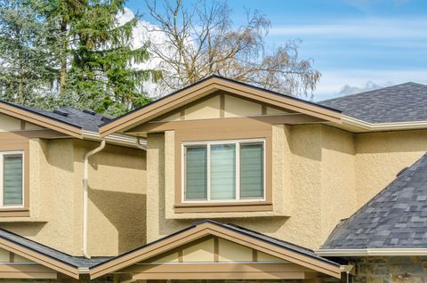 Beige stucco townhouse with gray shingle roof and central window under a blue sky