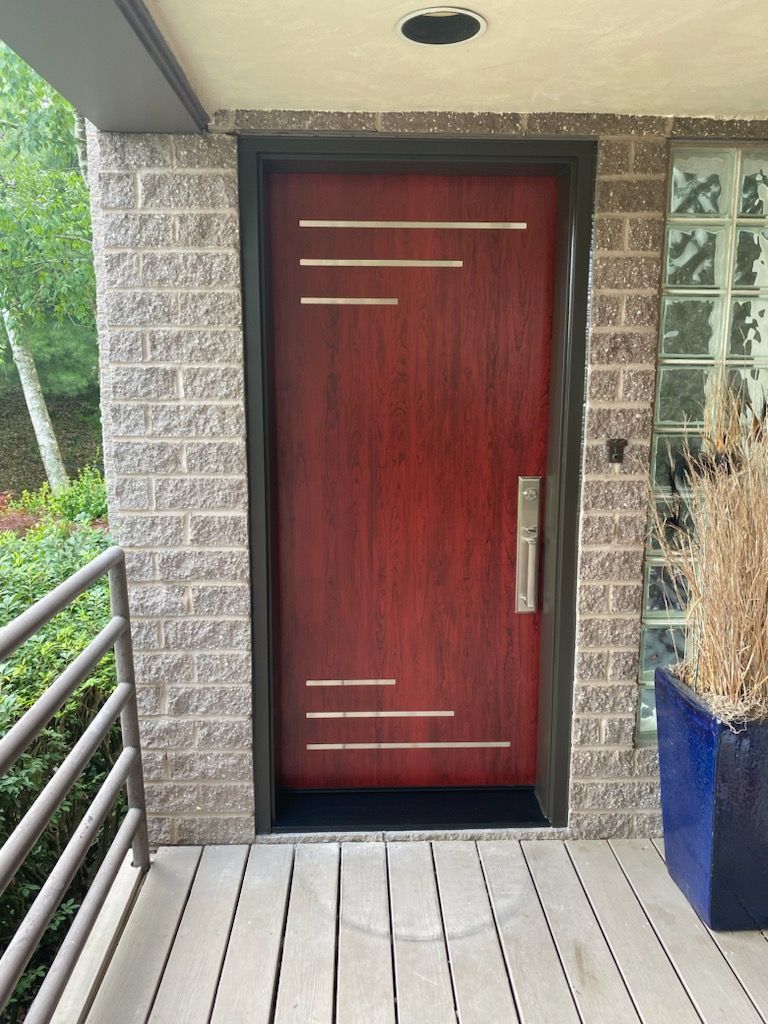 Red front door with horizontal gold stripes, brick wall, and blue planter.