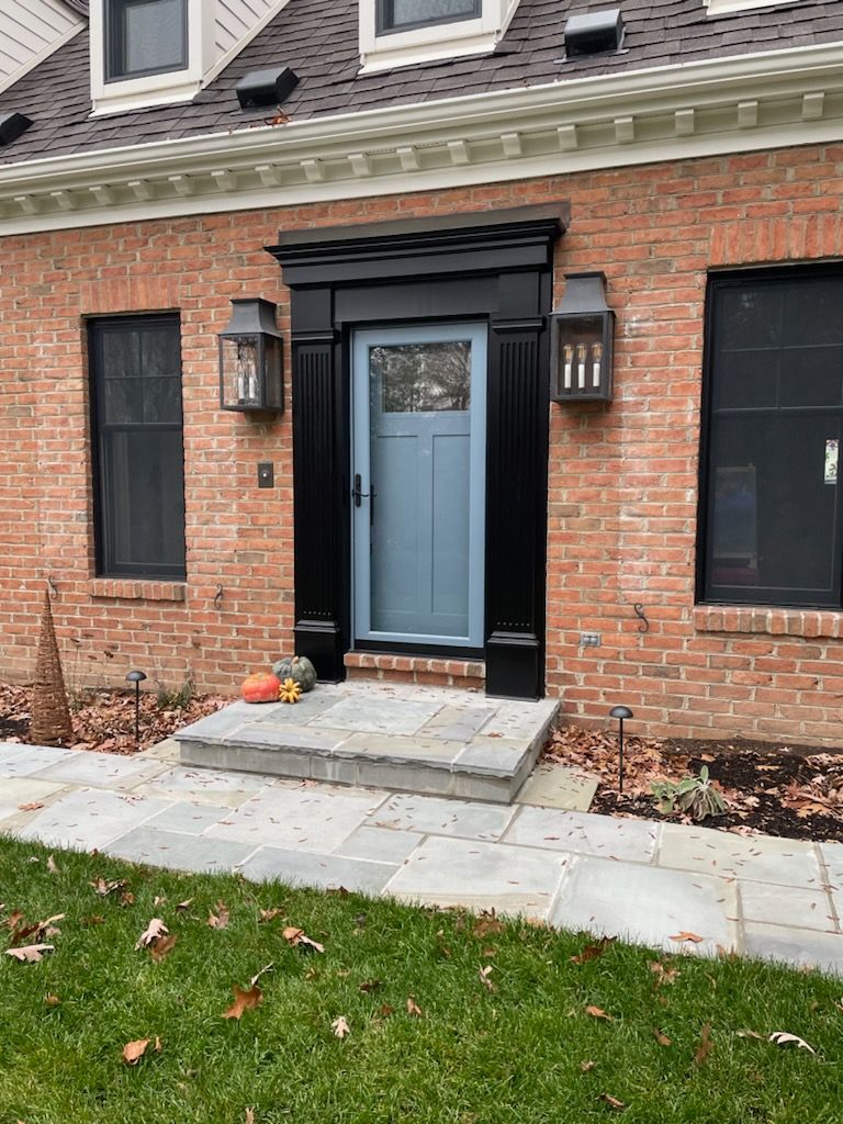 Brick house entrance with blue door, black trim, stone steps, and lanterns.