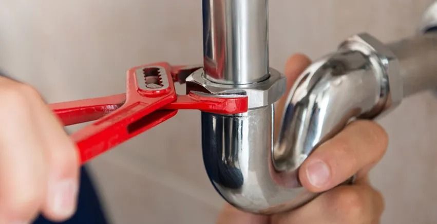 A person using a red wrench to tighten a silver pipe fitting.