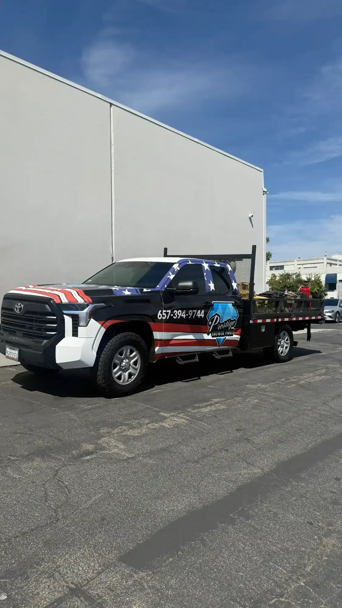 Truck with American flag wrap parked in front of a building on a sunny day.