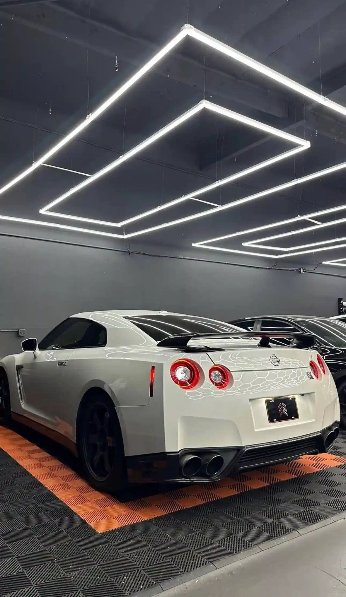 White Nissan GT-R sports car in a garage with geometric overhead lighting, angled view.