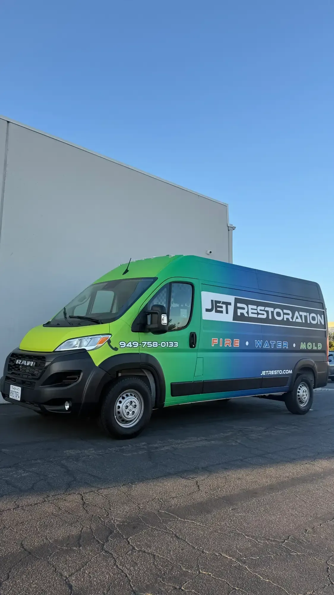 Green and blue JET Restoration van parked in front of a building on a sunny day.
