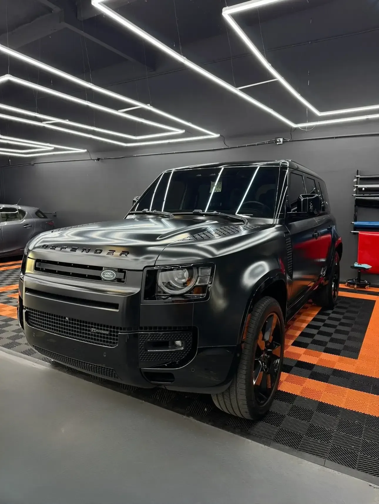 Black Land Rover Defender in a workshop with black and orange checkered flooring.
