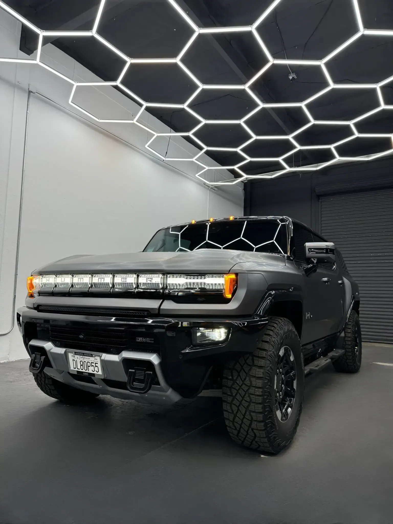 Black Hummer EV SUV parked in a showroom with hexagonal ceiling lights and a garage door.