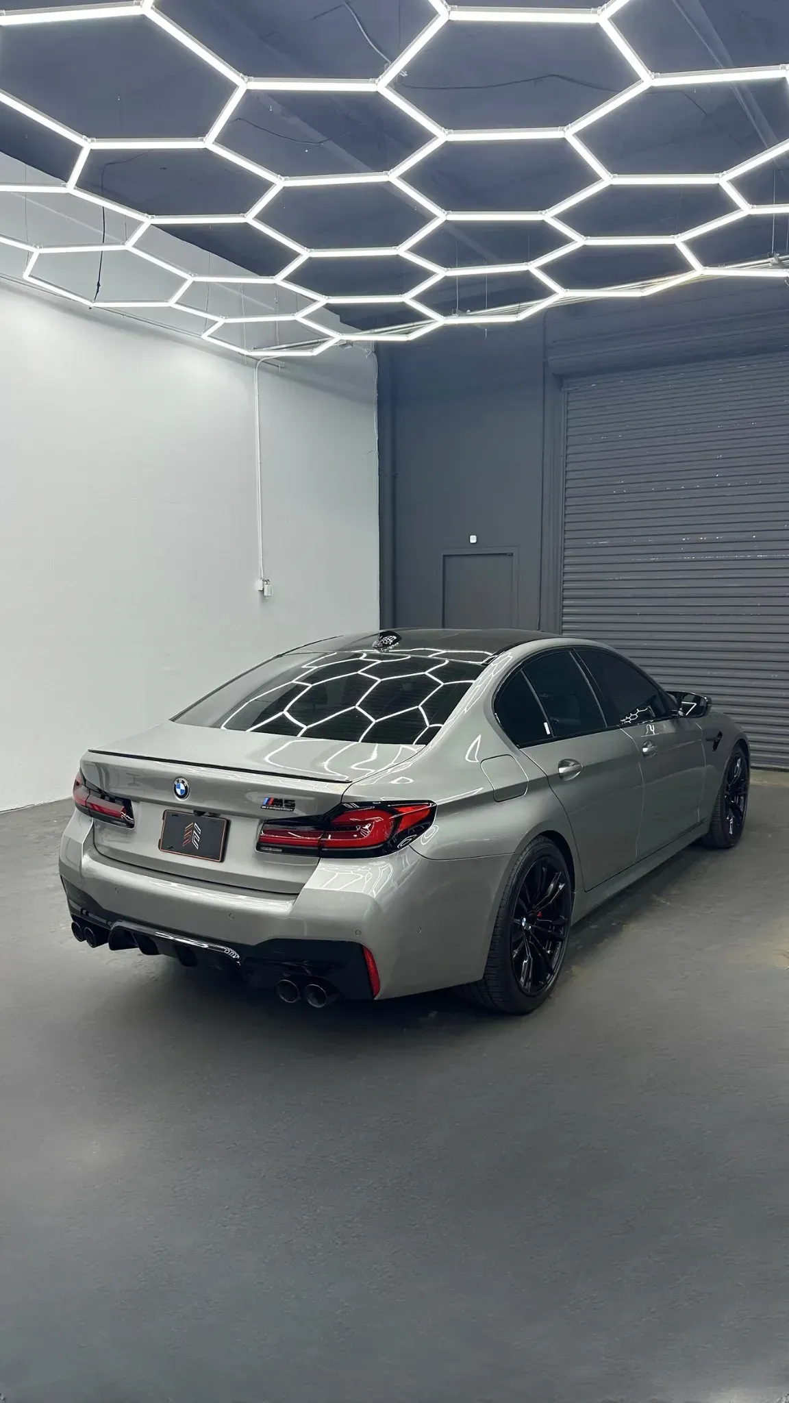 Silver BMW M5 sedan in a garage under hexagonal lights.