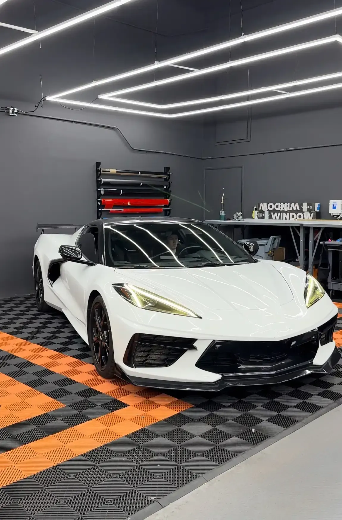 White sports car in a garage with black and orange flooring, black accents, and neon lights.