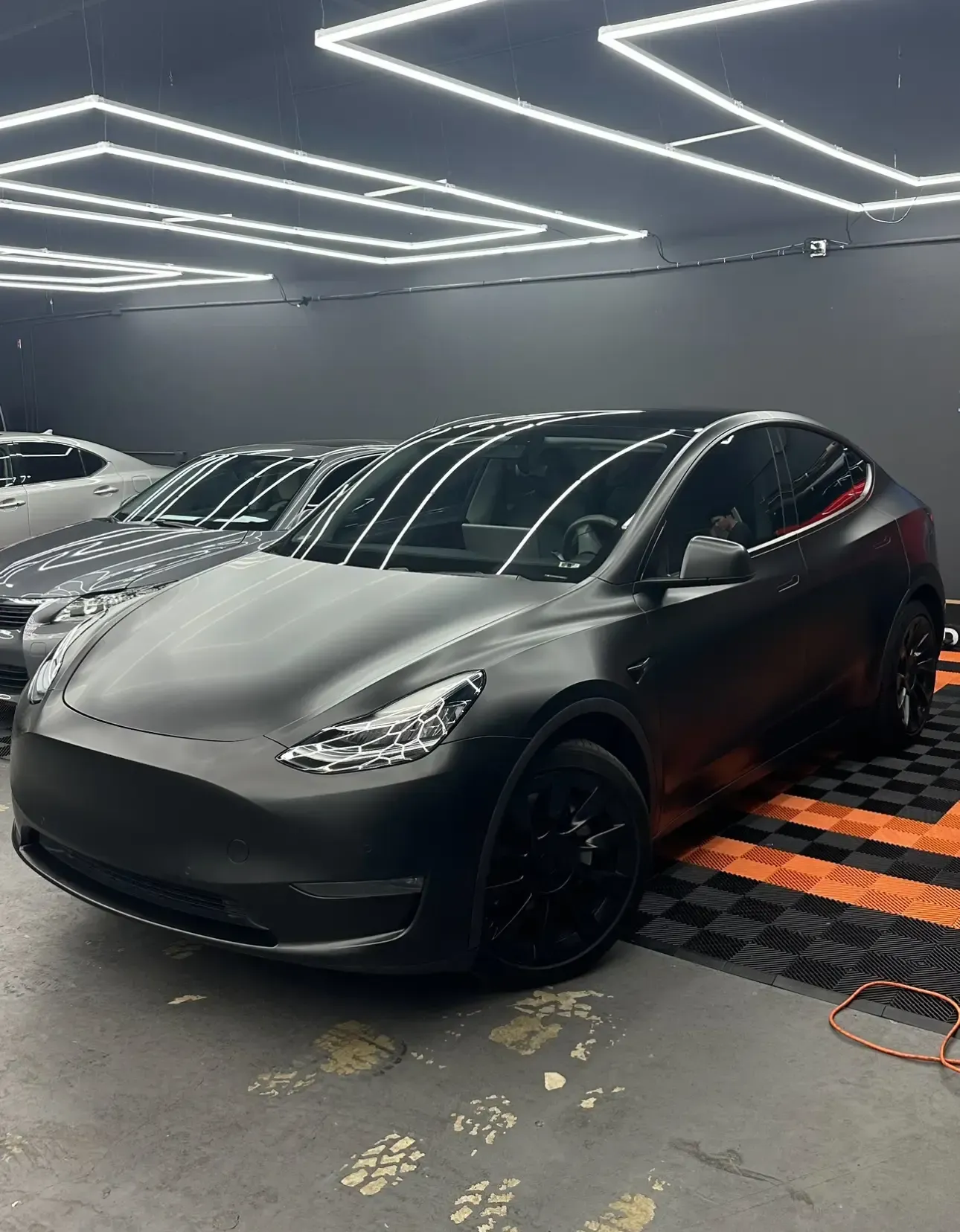 Black matte Tesla Model Y parked in a garage with other cars.