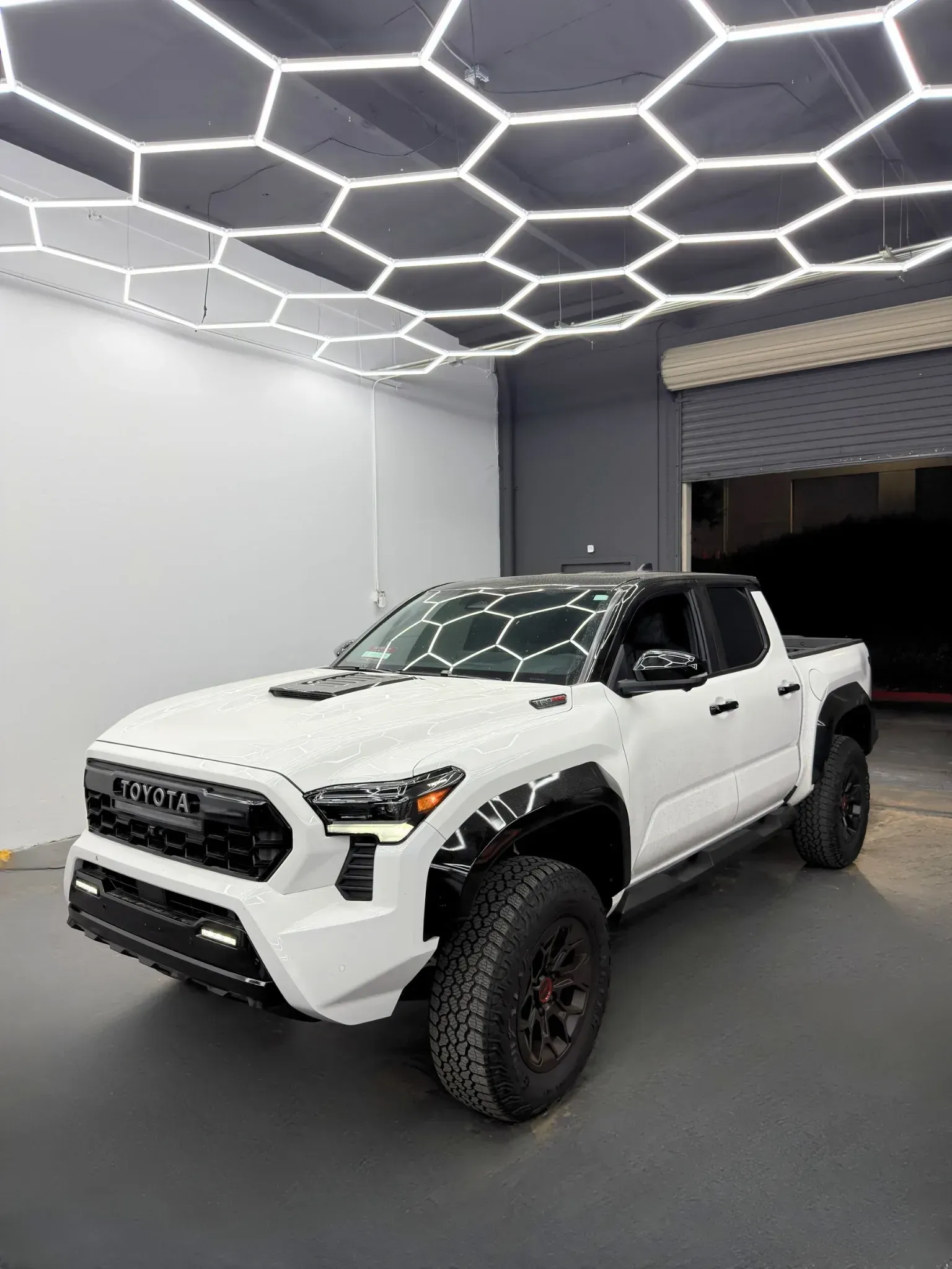 White Toyota Tacoma truck in a bright garage with honeycomb lights.