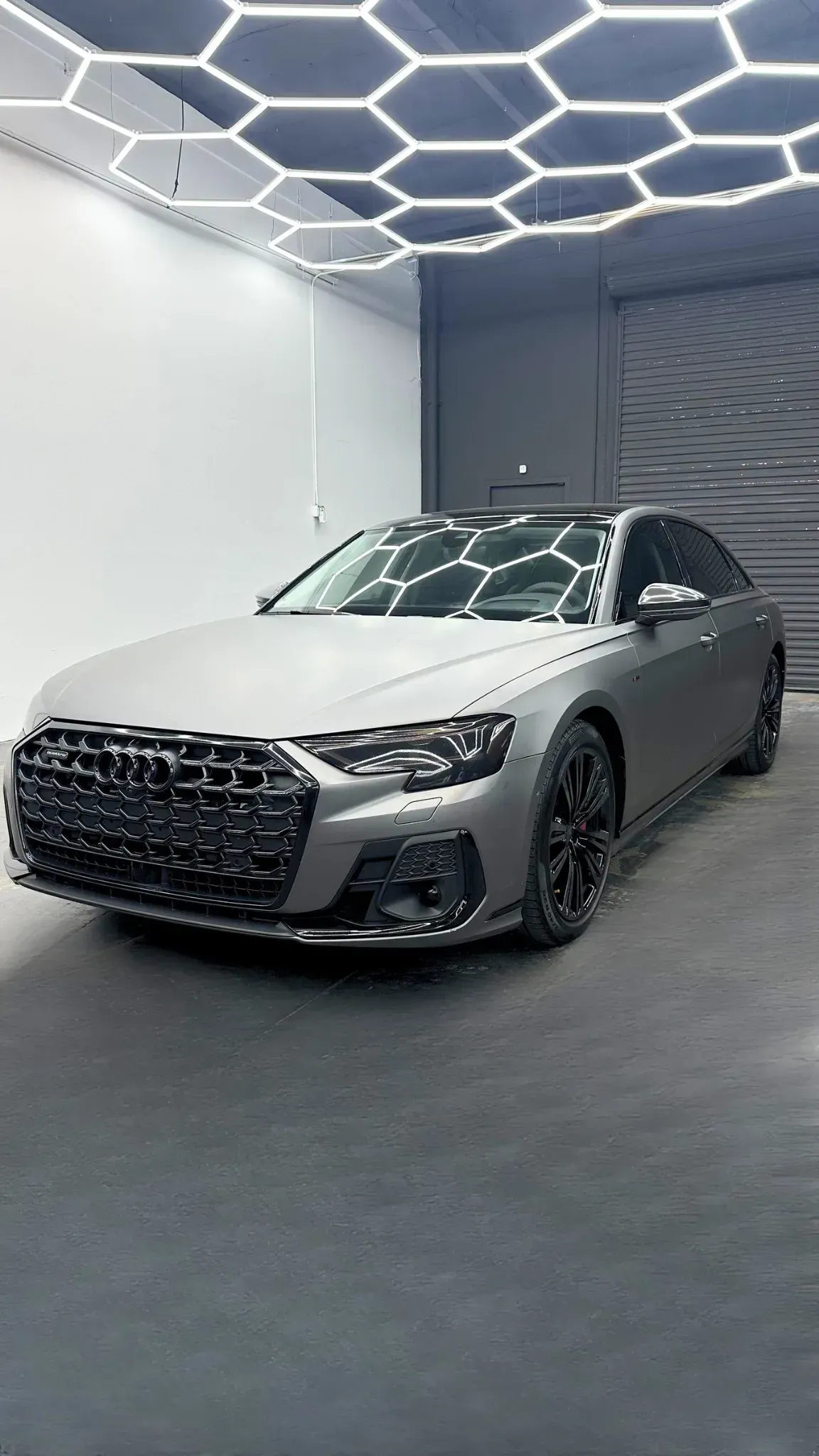 Gray Audi sedan in a brightly lit garage, under honeycomb-shaped lights.