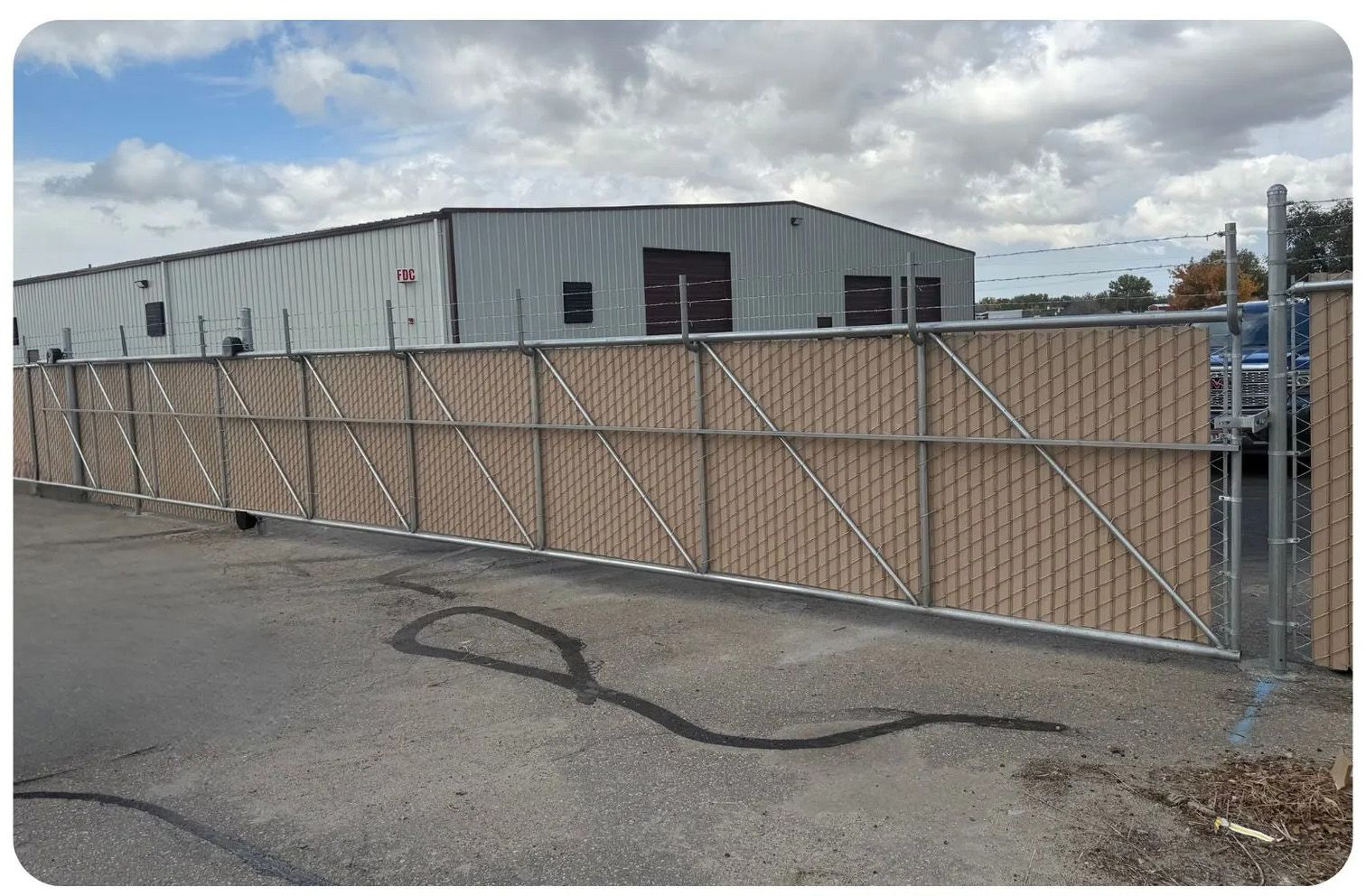 Tan privacy fence in front of a gray building on a cloudy day.