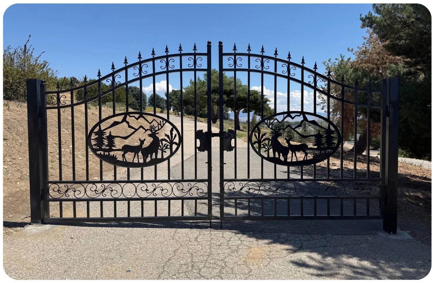 Black iron gate with deer and mountain scene cutouts, driveway entrance.