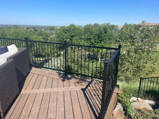 Wooden deck with black metal railing overlooking a green landscape and blue sky.