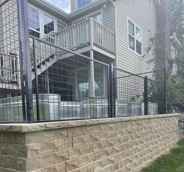 Black metal fence and galvanized stock tanks on a stone retaining wall against a house with a deck.
